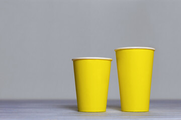 Mockup two yellow paper cups on grey background. Coffee cups and backdrop in the trending colors - ultimate grey and illuminating.