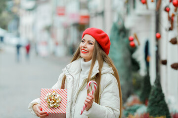 Christmas. Close-up portrait of a beautiful young woman in red biret holding a Christmas candy. Holidays.