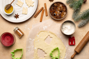 Process of making Christmas cookies with homemade dough,cookie cutters in the shape of tree and gift box,rolling pin,flour,cinnamon,cocoa powder and fresh eggs on beige table.Top view.