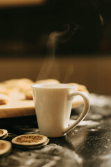 Vertical photo of a white cup with some steam on a black table near a wooden plate and some dried limes