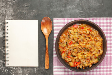 top view roasted eggplant salad in bowl a wooden spoon a notepad on dark background