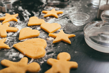Photo of some unbaked gingerbread figures on a black table with some flour