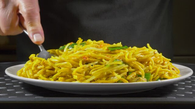 Closeup POV shot of a man using a fork to spread hot Chinese noodles on a plate, after just tipping the meal from a carton.