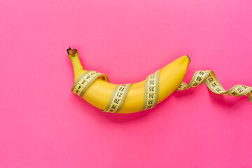 Yellow banana with measurement tape on pink background. Men penis size concept. Flat lay, top view, copy space.