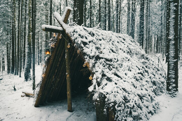 Primitive bushcraft survival shelter with Christmas garland bulbs in winter forest