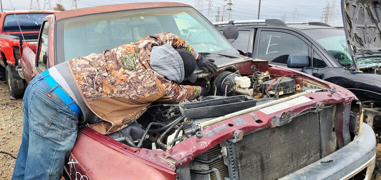 A man is taking the parts out of the car at a junkyard, Houston, Texas
