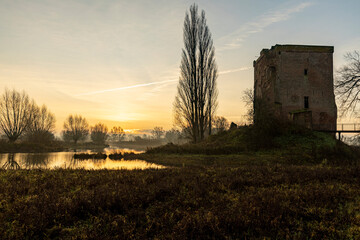 Early morning water and swamp landscape with the silhouette of the ruins of Nijenbeek castle in The Netherlands along the river IJssel at colorful winter sunrise