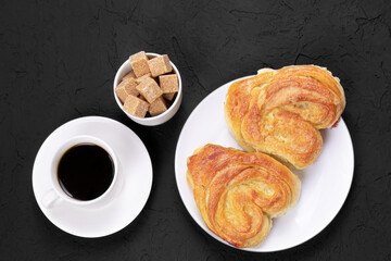Pastry on a white plate and cup of coffee on a black background. Homemade cake. Cane sugar. Fresh baked cake. Breakfast..
