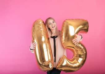 young happy girl holding large balloons in the form of the number fifteen on a pink background....