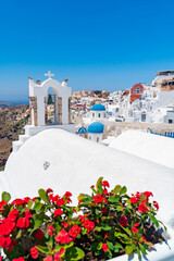 Red flowers bougainvillaea with background in Greek white orthodox church with bell tower on Santorini island, Oia, Cyclades, Greece