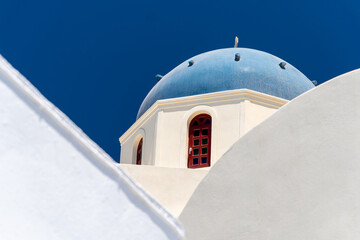 Old white greek church with blue dome on sky background on Santorini island. Greece. Brown window, low angle