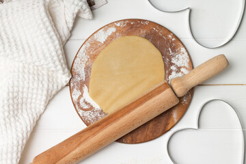 A heart-shaped cutout molds and rolled dough next to a towel and wooden spoons and rolling pin,...