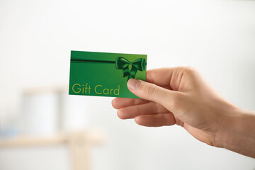 Woman holding gift card on blurred background, closeup