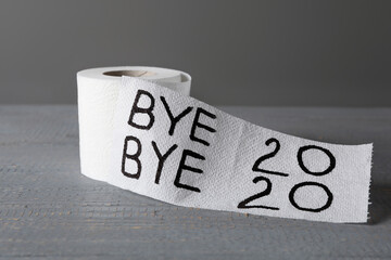 Toilet paper roll with text Bye Bye 2020 on light grey wooden background