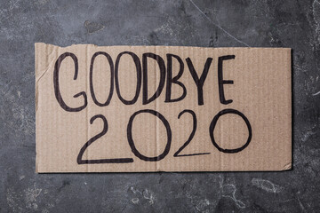 Cardboard with text Goodbye 2020 on grey stone background, top view