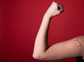 Female arm flexing bicep and making a fist wearing a bandage after receiving a Covid-19 Coronavirus...