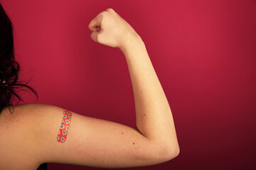 Female arm flexing bicep and making a fist wearing a bandage after receiving a Covid-19 Coronavirus vaccine injection