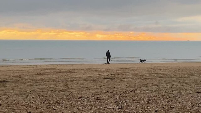 beach with man walking dog at sunset, Camber sands beach popular in summer with day trippers and winter with horse riders and dog walkers 
