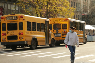 masked woman walking by school buses
