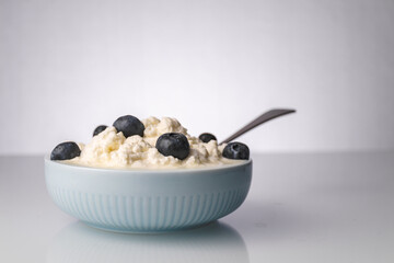 Whipped cheese with blueberries in a light blue ceramics bowl with a metal spoon in white background