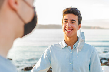 Obraz premium Young man smiling with surgical mask talking to a blurred person next to the sea