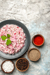 Vertical view of delicious chicken salad with mayonnaise and beet served with green on brown wooden cutting board and different spices lined up in a row on ice table