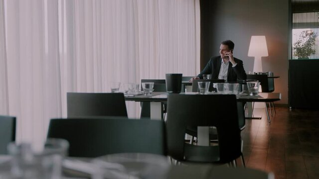 Businessman sitting in an empty restaurant and smiling while talking on the phone