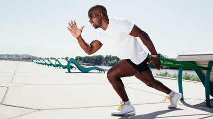 Black guy in white t-shirt and black shorts exercising and screaming outside with elastic tape.