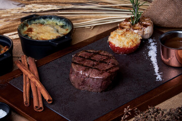 Grilled beef steak and side dishes on the wooden plate.