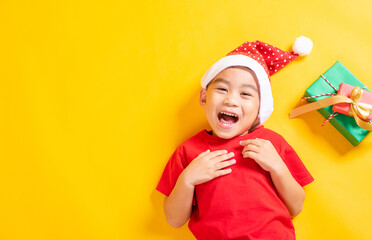 Asian little cute child boy smile, Top view of a kid dressed in red Santa Claus hat the concept of holiday Christmas Xmas day or Happy new year, isolated lying on yellow background