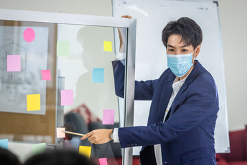 asian Business tomboy lesbian wearing protective mask presenting use post it notes to share idea.Brainstorming concept.Sticky note on glass wall in the meeting room at office,Concept of COVID-19