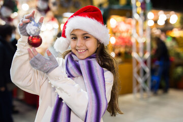 Happy teenage girl demonstrating christmas balls at street christmas market