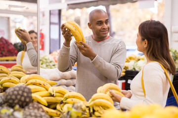 Married couple picks and buys ripe bananas in the vegetable section of a grocery supermarket