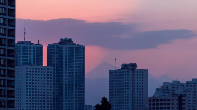 Breathtaking Sunrise Behind the Damavand Alone Volcano Mountain Peak in Tehran Iran with Shadow of Sun Ray Behind The Buildings Silhouette in Yellow Orange Sky Early Morning with some Clouds