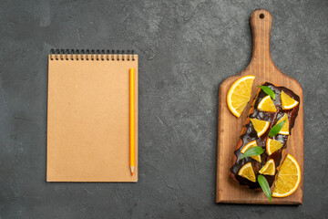 Above view of delicious cakes decorated with lemon and chocolate on cutting board next to notebook