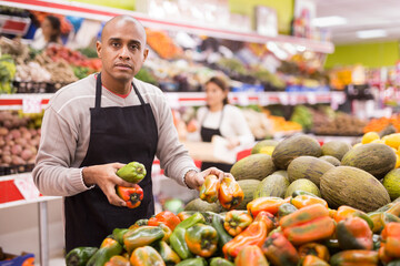 Supermarket employee in apron checking products in vegetable department