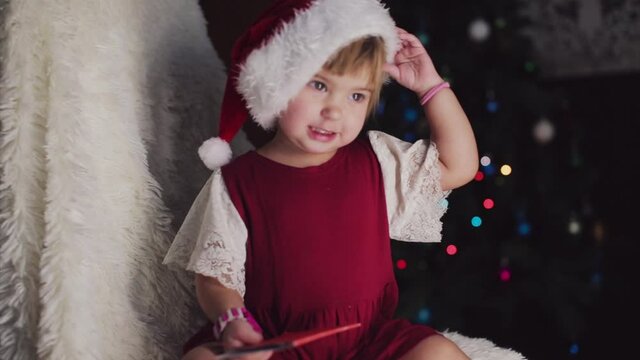 a child in red clothes is sitting waiting for the new year. the concept of celebrating Christmas at midnight. holiday costume. a girl writes a letter to Santa Claus. wish list