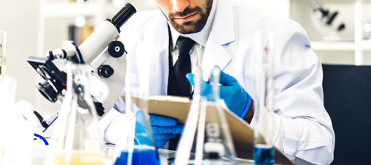 Fototapeta premium Professional scientist man research and working doing a chemical experiment while making analyzing and mixing liquid in test tube.Young science man looking sample chemical on glass at laboratory