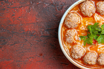 Half shot of meatballs soup with noodles in a brown bowl on the left side of dark background