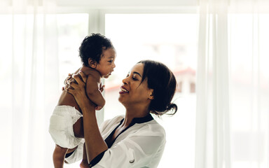 Portrait of enjoy happy love family african american mother playing with adorable little african american baby.Mom touching with cute son moments good time in a white bedroom.Love of black family 