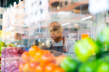 Seller in supermarket of Latin American origin checking product .Foreground of glass display case