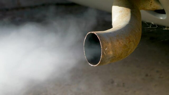 Closeup POV shot of fumes / smoke belching from the rear exhaust tail pipe of an old classic / vintage  car, just after being started, with water in the pipe due to the cold.