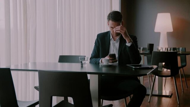 Businessman sitting at an empty table and typing on his phone with a concern face