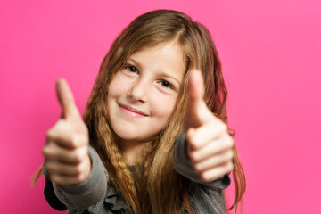 Front view portrait of young small caucasian girl eight years old posing in front of pink background with thumbs up gesture - confidence support and success concept