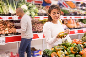 Adult latin american woman choosing sweet pepper in supermarket with other buyer