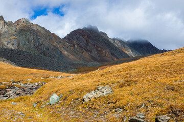Dry yellow grass on the rocky mountain slope with heavy fog. Autumn mountain landscape.
