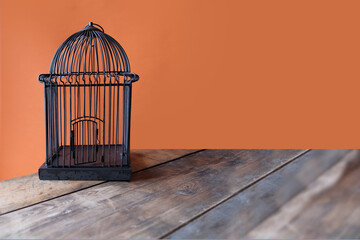 black empty bird cage stands on an old wooden table, orange background, space for designer, concept...