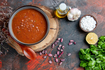 Classic tomato soup in a blue bowl spoon on wooden tray oil bottle garlic salt and lemon a bunch of green on mixed color background