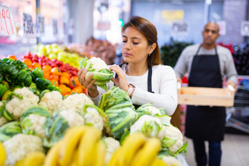Salesgirl standing near fresh cauliflower and vegetables in grocery store
