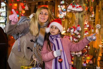 Obraz na płótnie Canvas Happy daughter with mom point finger at selected christmas tree decorations at street christmas market